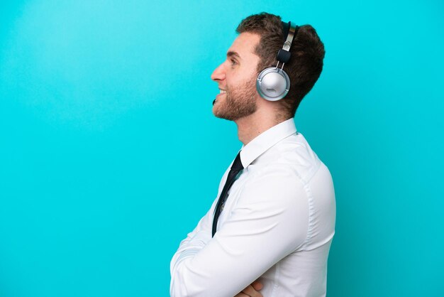 Telemarketer caucasian man working with a headset isolated on blue background in lateral position