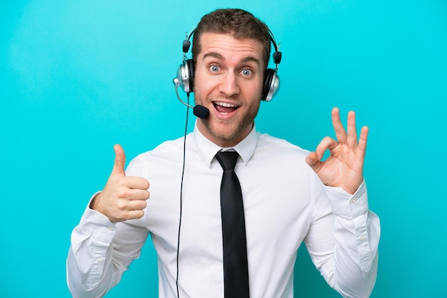 Telemarketer caucasian man working with a headset isolated on blue background showing ok sign and thumb up gesture