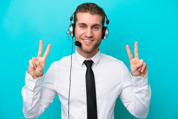 Telemarketer caucasian man working with a headset isolated on blue background showing victory sign with both hands