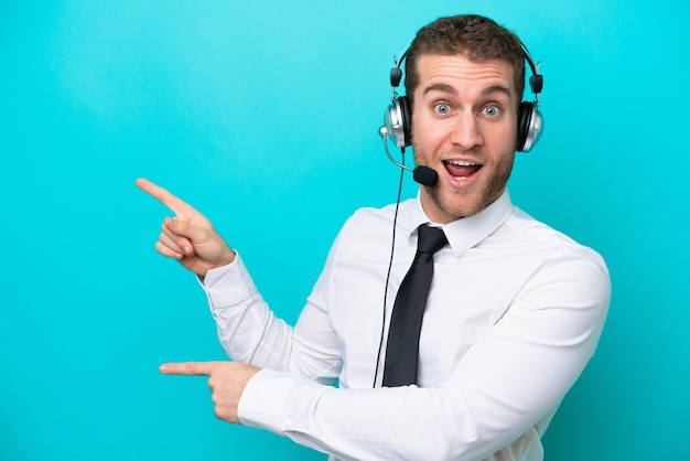 Telemarketer caucasian man working with a headset isolated on blue background surprised and pointing side