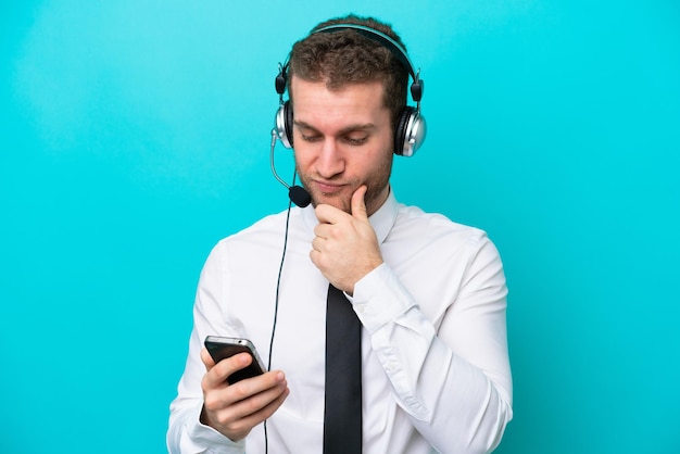 Telemarketer caucasian man working with a headset isolated on blue background thinking and sending a message