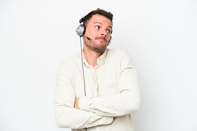 Telemarketer caucasian man working with a headset isolated on white background making doubts gesture while lifting the shoulders