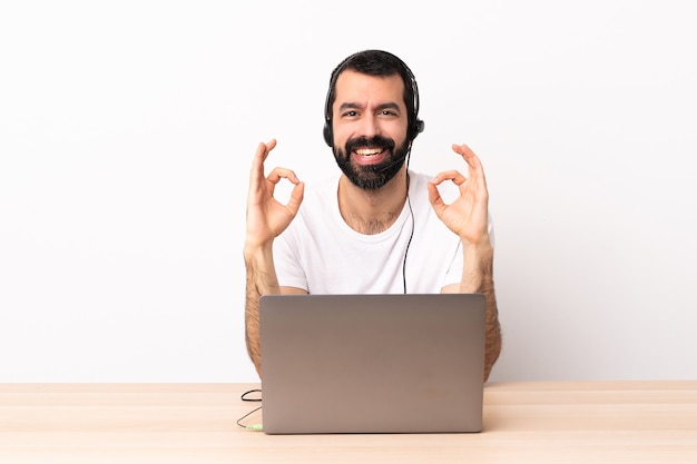 Telemarketer caucasian man working with a headset and with laptop showing ok sign with two hands.