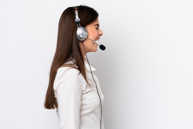 Telemarketer caucasian woman working with a headset isolated on white background laughing in lateral position