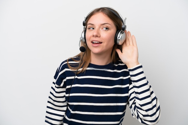 Telemarketer caucasian woman working with a headset isolated on white background listening to something by putting hand on the ear