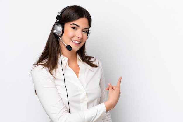 Telemarketer caucasian woman working with a headset isolated on white background pointing back