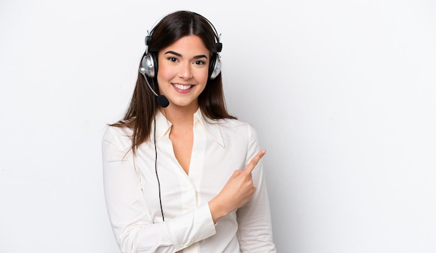 Telemarketer caucasian woman working with a headset isolated on white background pointing to the side to present a product