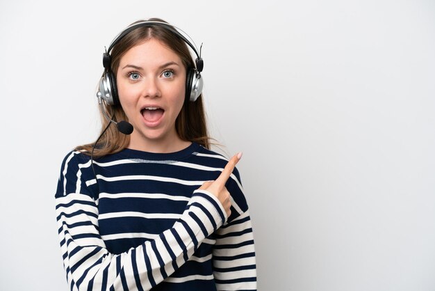 Telemarketer caucasian woman working with a headset isolated on white background surprised and pointing side