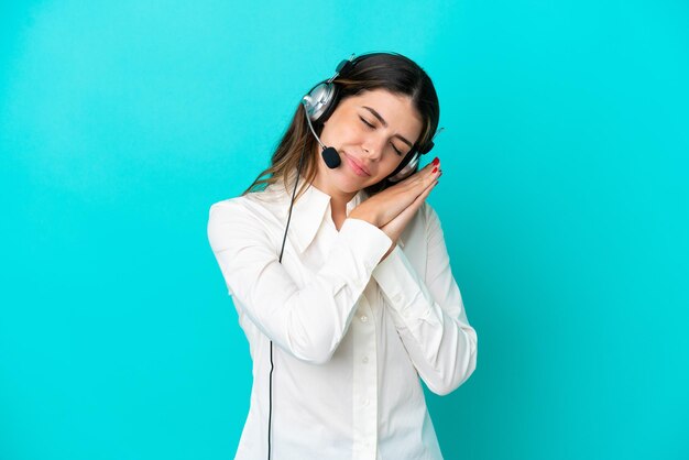 Telemarketer Italian woman working with a headset isolated on blue background making sleep gesture in dorable expression