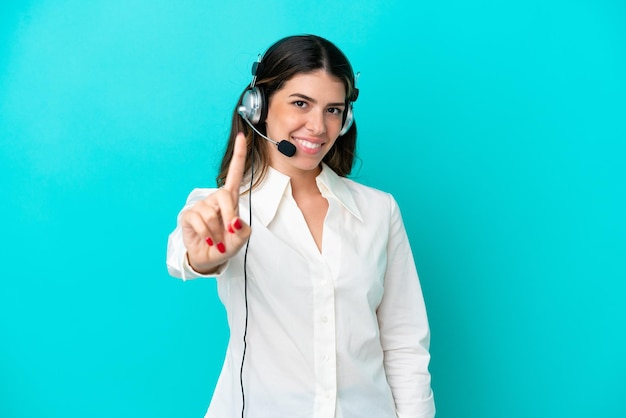 Telemarketer Italian woman working with a headset isolated on blue background showing and lifting a finger