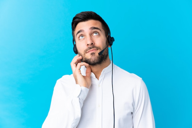 Telemarketer man working with a headset over blue thinking an idea