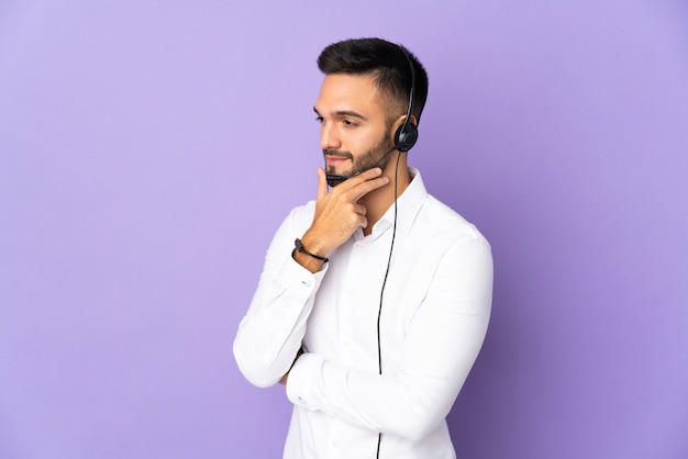 Telemarketer man working with a headset isolated on purple background looking to the side and smiling