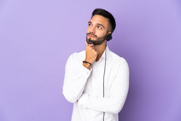 Telemarketer man working with a headset isolated on purple background and looking up