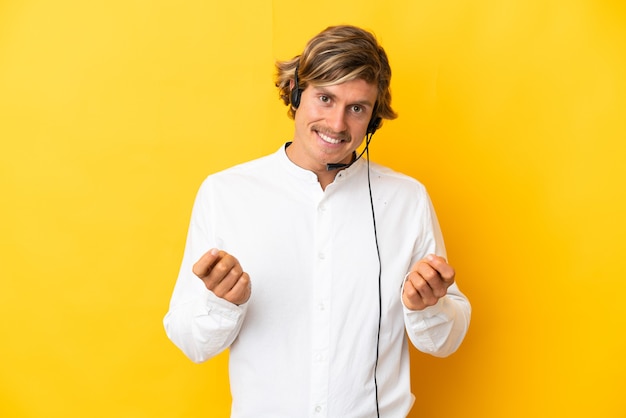 Telemarketer man working with a headset isolated on yellow wall making money gesture