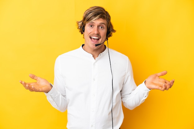 Telemarketer man working with a headset isolated on yellow with shocked facial expression