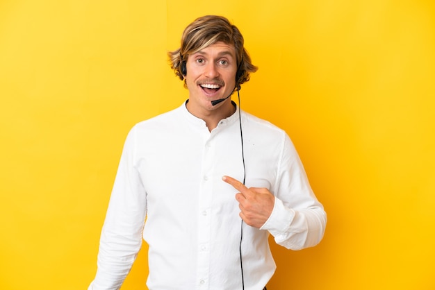 Telemarketer man working with a headset isolated on yellow with surprise facial expression