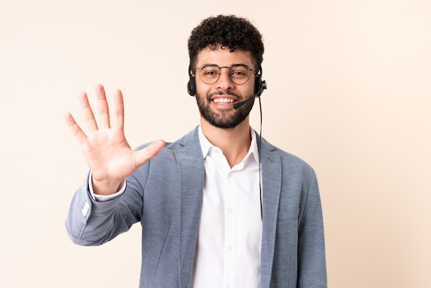 Telemarketer Moroccan man working with a headset isolated on beige wall counting five with fingers