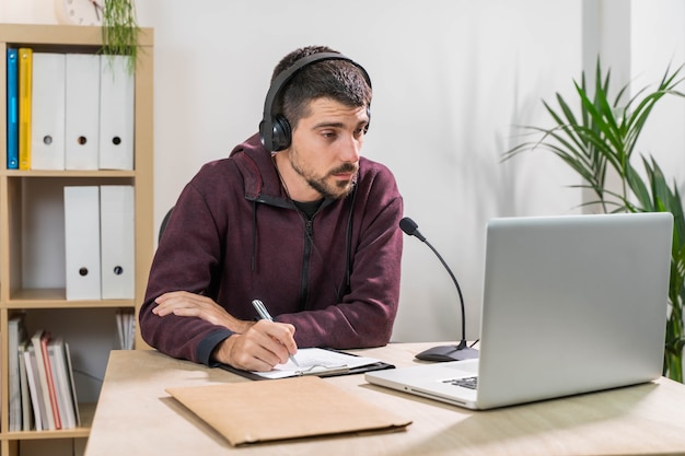 Telemarketer or podcast man working with laptop and talking on a headset with face mask at office