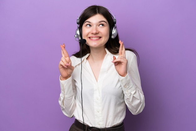 Telemarketer Russian woman working with a headset isolated on purple background with fingers crossing