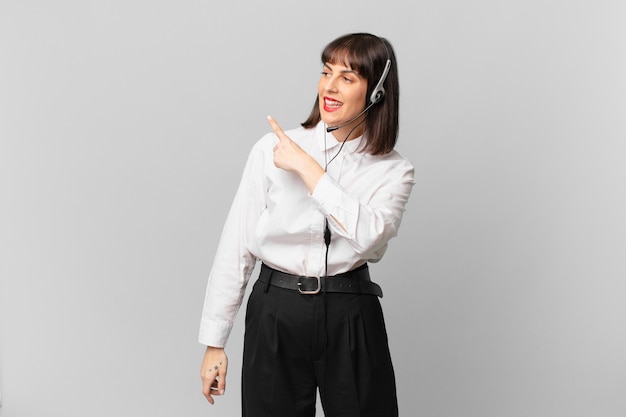 Telemarketer woman looking excited and surprised pointing to the side and upwards to copy space