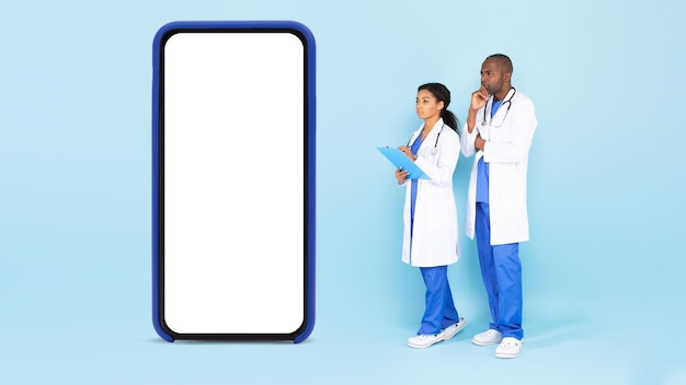 Telemedicine concept Doctors standing near big blank smartphone and looking at white screen mockup