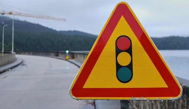 Temporary traffic light warning sign for construction, with view of green traffic light and crane