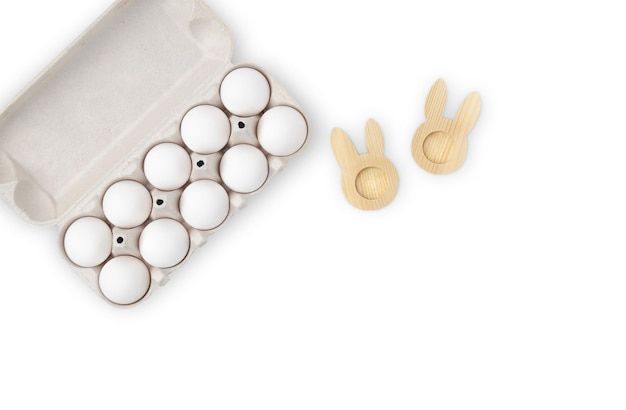 Ten white eggs in a cardboard box and an egg stand in the form of a rabbit on a white background