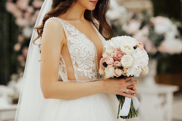 Tender bride holds a bouquet with white and pink roses in her hands.