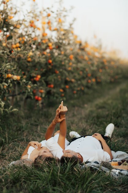 Tender couple lying on the green grass and holding hands up. Young couple are having picnic in the apples orchard.