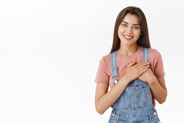 Tender, feminine lovely happy woman in overalls, t-shirt, press hands to heart, tilt head and smiling thanking dearly for help, looking grateful, appreciate effort, express gratitdue, touched