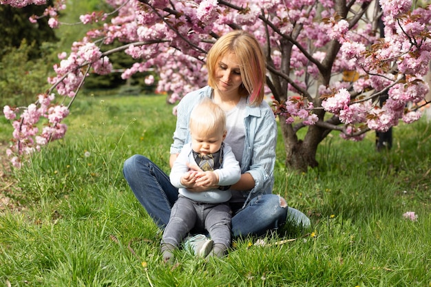 Tender happy mother in a blue shirt sitting with a baby son in spring Motherhood and femininity