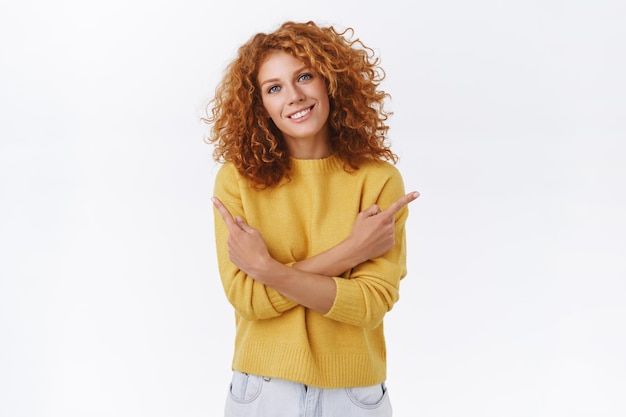 Tender, lovely caucasian redhead curly girl in yellow sweater, cross arms over chest and pointing sideways