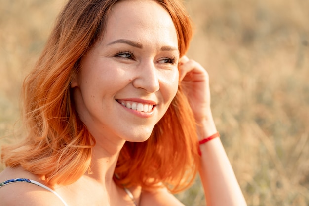 Tender red-haired woman enjoys the sunset in a field with a hill.