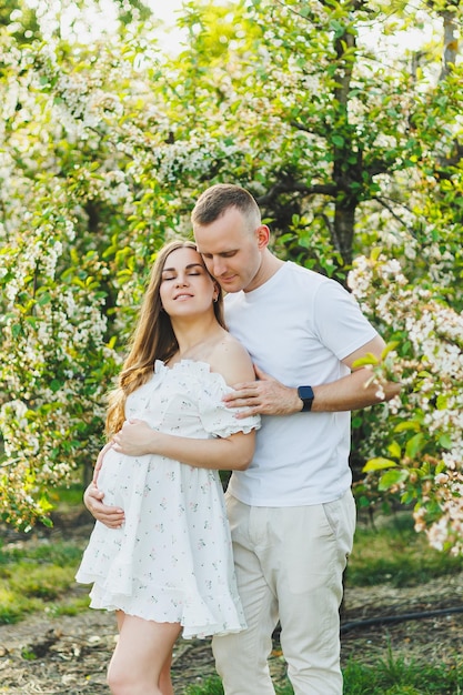 Tender romantic pregnant couple hugging in blooming apple spring garden Expectant parents in the park of white flowering trees A couple is expecting a baby