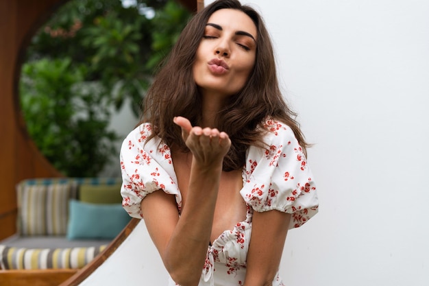 Tender soft romantic fashion portrait of tanned fit skinny woman posing by white wall outdoor wearing sexy stylish dress