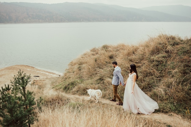 Tender wedding couple in love in the autumn forest with a dog is walking near the lake