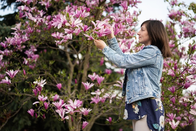 Tender woman in jeans jacket enjoying nice spring day near magnolia blooming tree Springtime activities