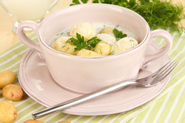 Tender young potatoes with sour cream and herbs in pan on wooden table closeup