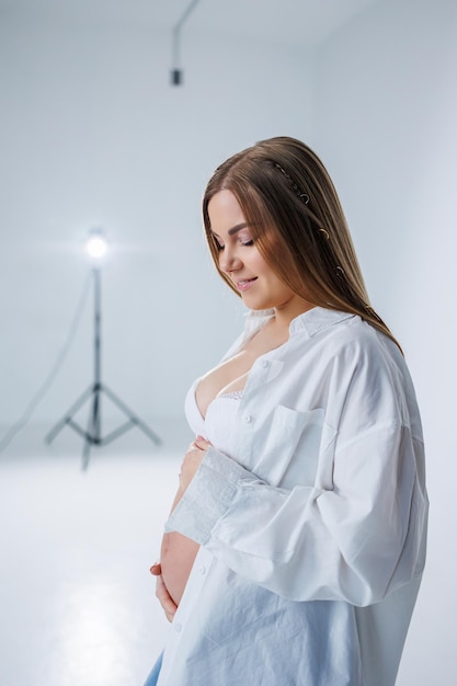 A tender young pregnant woman in a white shirt and jeans hugs her belly Pregnant happy woman on a white background