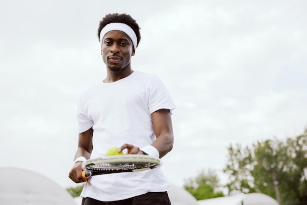 Tennis player of african appearance is standing on tennis court holding racket