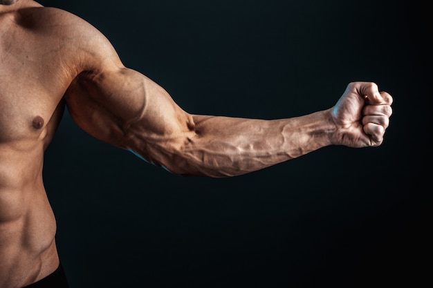 Tense arm clenched into fist, veins, bodybuilder muscles on a dark space, isolate