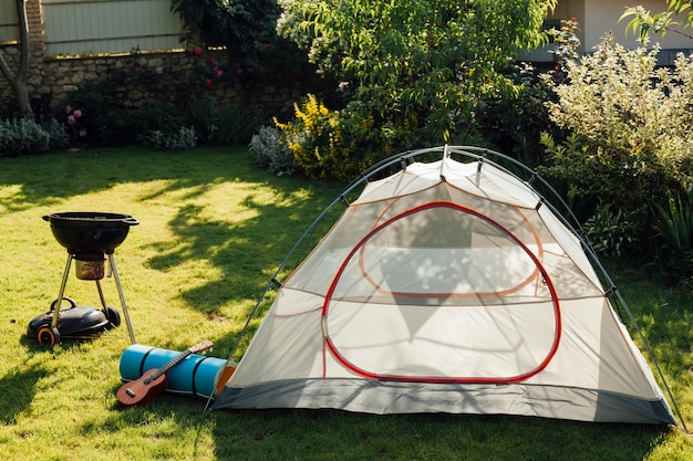 Tent camping with barbecue grill and ukulele on grass