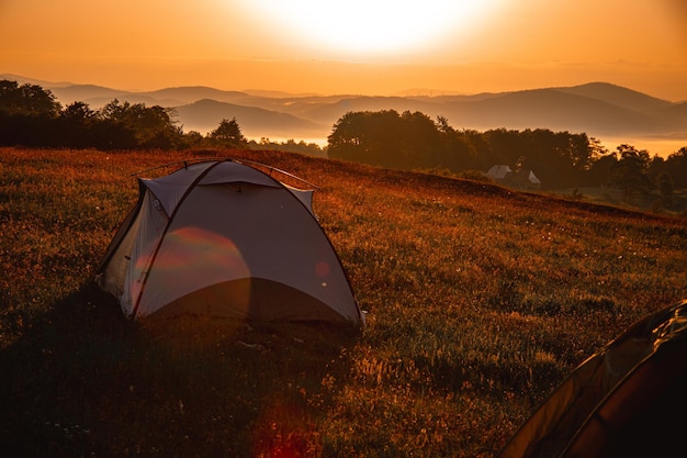 Tent on a hill covered in greenery during a beautiful bright sunrise in the morning