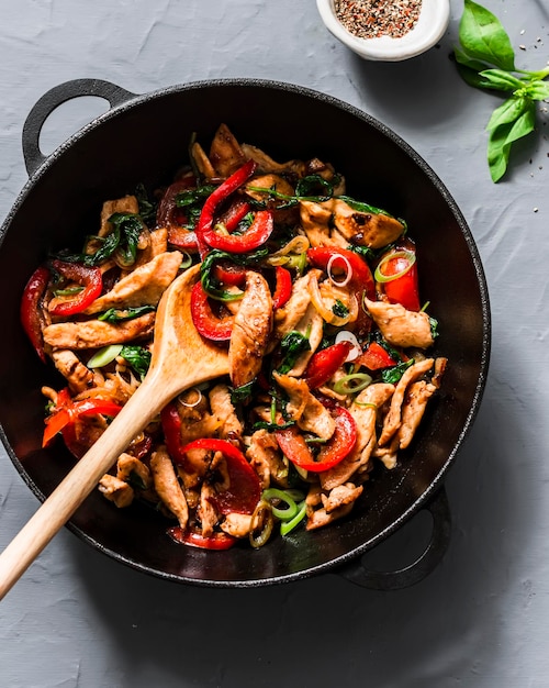 Teriyaki chicken bell peppers onions and spinach stir fry in a pan on a gray background top view