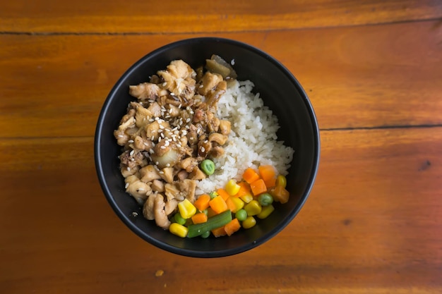 Teriyaki chicken rice bowl with vegetables and corn on wooden background