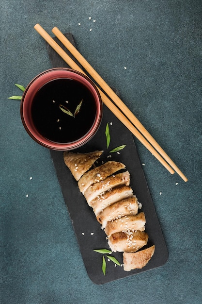 Teriyaki chicken slices on a graphite black board with chopsticks and soy sauce on a dark background. Asian food. Vertical orientation. Top view with a copy space for the text.