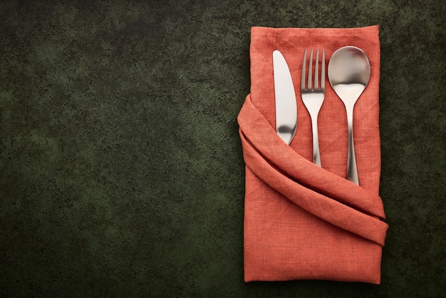 Terracottacolored linen napkin folded in the shape of a pocket with cutlery inside dark green background with copy space