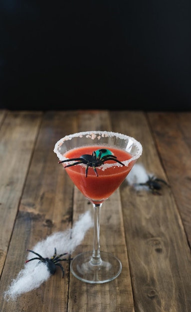 Terrifying red cocktail with spider on black background and wooden Halloween table with decoration Vertical