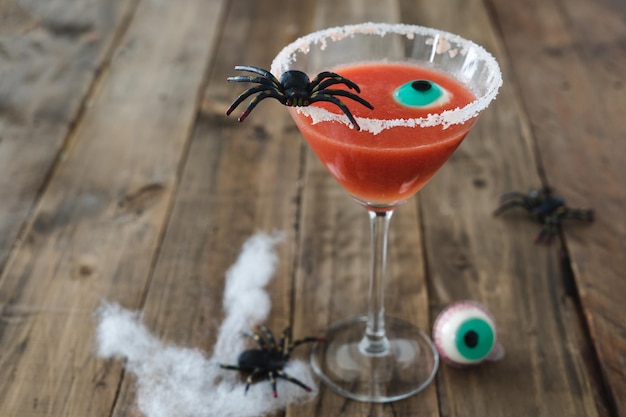 Terrifying red cocktail with spider on wooden background for Halloween with decoration Photo vertical