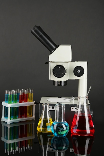 Test tubes with colorful liquids and microscope on dark grey background